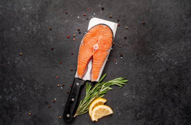 Çiğ balık somon bifteği, arka planda et bıçağının üzerinde malzemeler var.