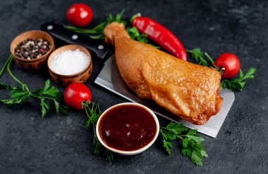 Et bıçağında tütsülenmiş tavuk budu ve arka planda baharatlar.