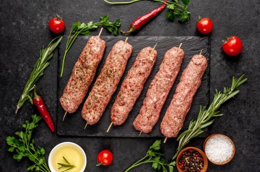 Şişler üzerinde çiğ Lula kebabı ve arka planda baharatlar.