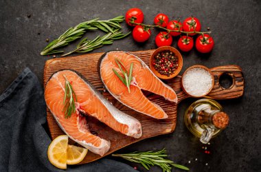 Çiğ balık somon bifteği ve taştan bir arka planda kesim tahtası malzemeleriyle yakın plan görüntüsü.