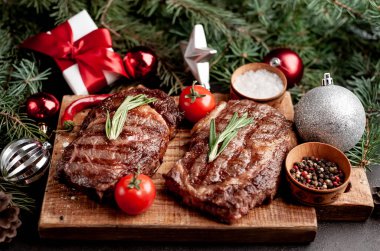 İki kişilik Noel yemeği, ızgara biftek, pirzola, yeşillik ve baharatlar bir taş masanın üzerinde Noel ağacı ve yeni yıl oyuncakları süslemesi.
