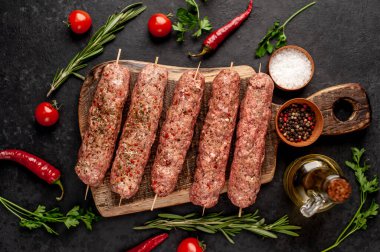 Şiş üzerinde çiğ Lula kebabı ve taş zeminde baharat kesme tahtası.