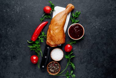 Et bıçağında tütsülenmiş tavuk budu ve arka planda baharatlar.