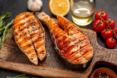 Izgara somon bifteği ve taştan bir arka planda kesim tahtası malzemeleriyle yakın plan görüntüsü.