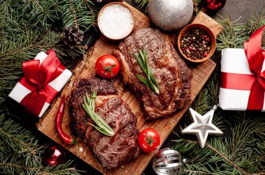 İki kişilik Noel yemeği, ızgara biftek, pirzola, yeşillik ve baharatlar bir taş masanın üzerinde Noel ağacı ve yeni yıl oyuncakları süslemesi.