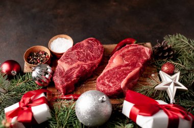 Noel tatili için iki kişilik yemek hazırlamak için çiğ pirzola bifteği ve Noel ağacı ve süslemeleri olan taş bir masada.