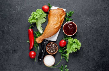 Et bıçağında tütsülenmiş tavuk budu ve arka planda baharatlar.