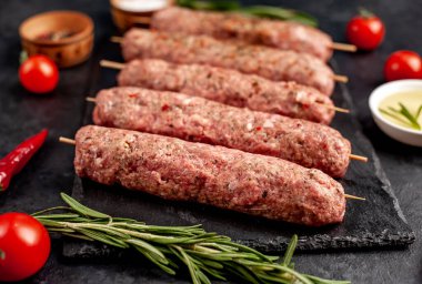 Şişler üzerinde çiğ Lula kebabı ve arka planda baharatlar.