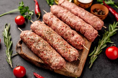 Şiş üzerinde çiğ Lula kebabı ve taş zeminde baharat kesme tahtası.