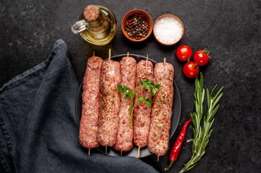 Siyah tabakta baharat ve arka planda taş kaplama şiş üzerinde ham Lula kebabı.