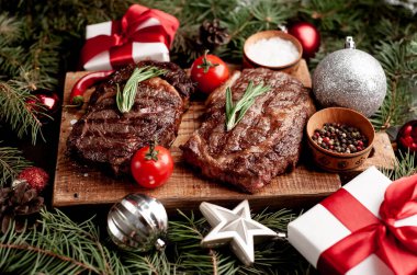 İki kişilik Noel yemeği, ızgara biftek, pirzola, yeşillik ve baharatlar bir taş masanın üzerinde Noel ağacı ve yeni yıl oyuncakları süslemesi.