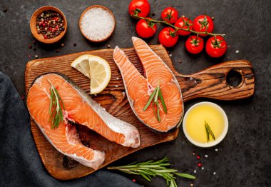 Çiğ balık somon bifteği ve taştan bir arka planda kesim tahtası malzemeleriyle yakın plan görüntüsü.