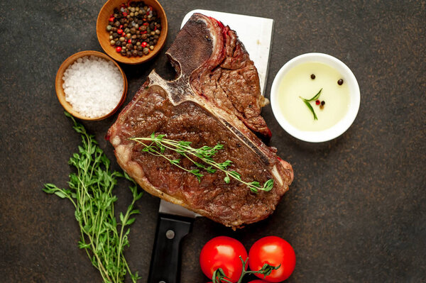 Grill t-bone steak with ingredients on a meat knife on stone background