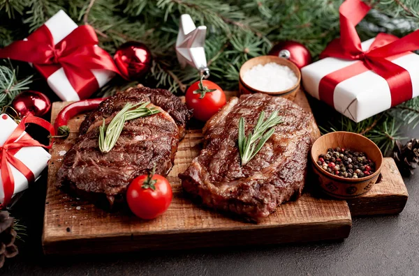 İki kişilik Noel yemeği, ızgara biftek, pirzola, yeşillik ve baharatlar bir taş masanın üzerinde Noel ağacı ve yeni yıl oyuncakları süslemesi.