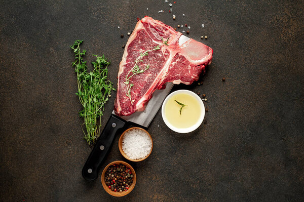 closeup view of raw t-bone steak with ingredients on a meat knife  on stone background