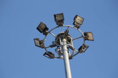 Mavi gökyüzünde spot ışıklarıyla dolu büyük bir elektrik direği