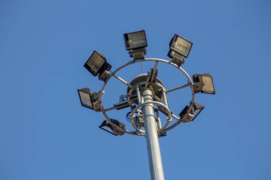 Mavi gökyüzünde spot ışıklarıyla dolu büyük bir elektrik direği