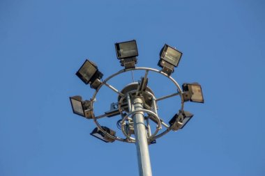 Mavi gökyüzünde spot ışıklarıyla dolu büyük bir elektrik direği