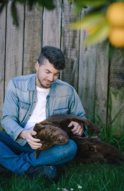 Çimenlerde oturan bir adam bahçede köpeğiyle oynuyor. Dikey fotoğrafçılık