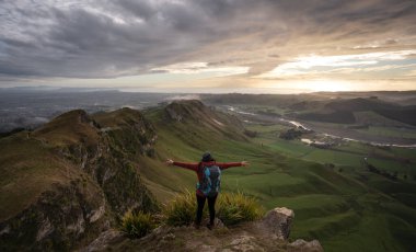 Sırt çantalı kadın bir dağın zirvesinde dururken kollarını açıyor. Seyahat kavramı