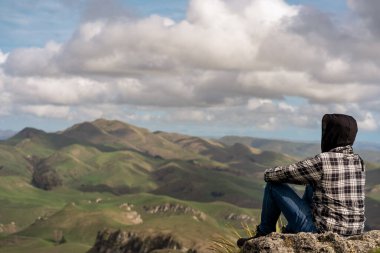 Kafkasyalı genç adam dağın tepesinde oturuyor ve manzarayı inceliyor..