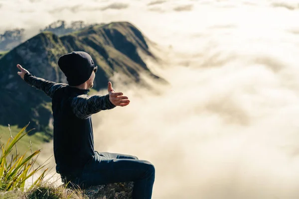 年轻人坐在山顶上 在一个雾蒙蒙的早晨张开双臂 旅行概念 — 图库照片