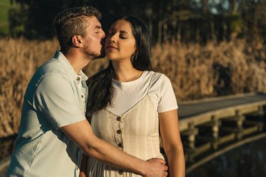 Gün batımında göl kıyısında bir adam kız arkadaşını yanağından öpüyor. Portre fotoğrafçılığı, kopyalama alanı