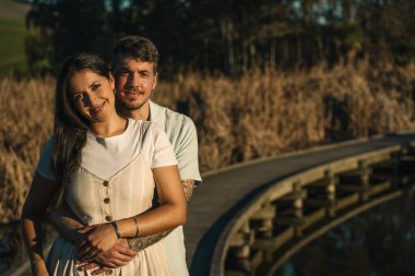 Genç çift kameraya bakıyor ve doğal ortamda poz veriyor tahta kaldırımlar, akıntılar ve bir göl ile. Romantizm kavramı