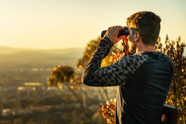 Dağın tepesinde gözcülük yapan ve dürbünle izleyen bir adam.