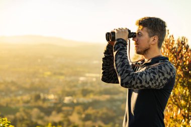 Genç adam, dağların ortasında dürbün kullanıyor. Yatay nazlı boşluk