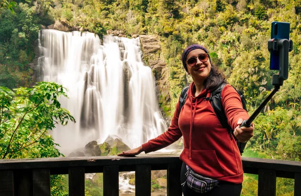 自撮り棒で滝で自撮りしている若い女性 ソーシャルメディアと旅行のコンセプト — ストック写真