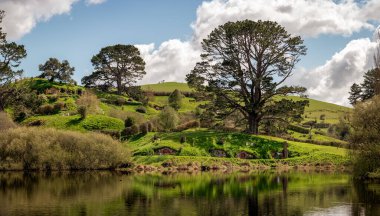 Gölün üzerindeki Hobbiton bölgesinin panoramik manzarası. Hobbiton Film Seti Turu. Eylül 2020, Matamata, Yeni Zelanda. Yüzüklerin Efendisi ve Hobbit Filmleri.
