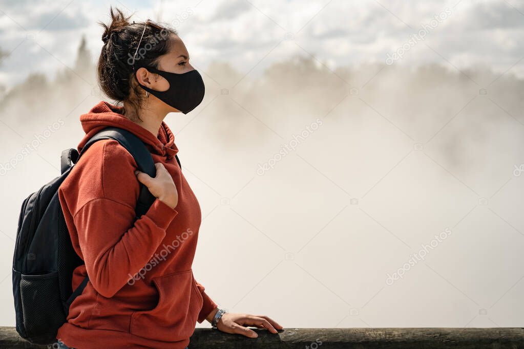 Young hispanic woman wearing face mask and touring on city with thermal activity. New Tourism and Coronavirus concept.