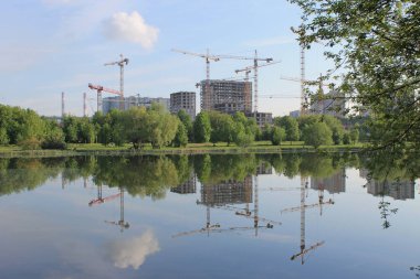 Sabahın erken saatlerinde mavi gökyüzüne karşı vinçli konut ların inşaatı ve gölete yansıtılması