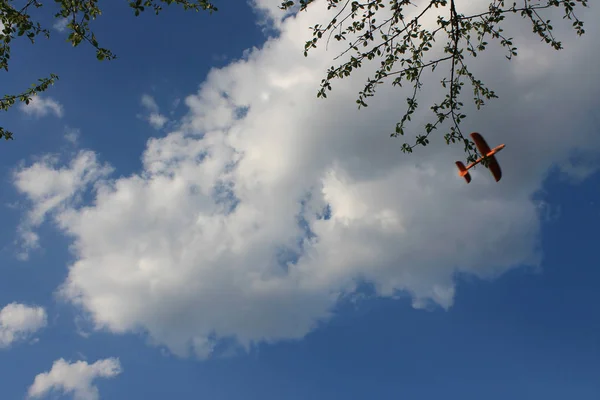Orange foam airplane floating in the air against the background of white clouds and blue sky
