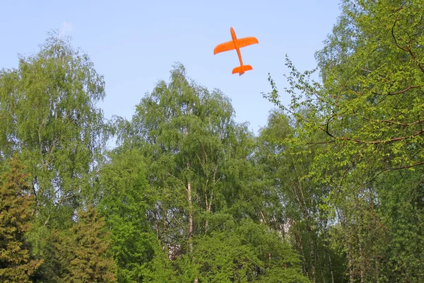 Orange foam airplane floating in the air against the background of white clouds and blue sky