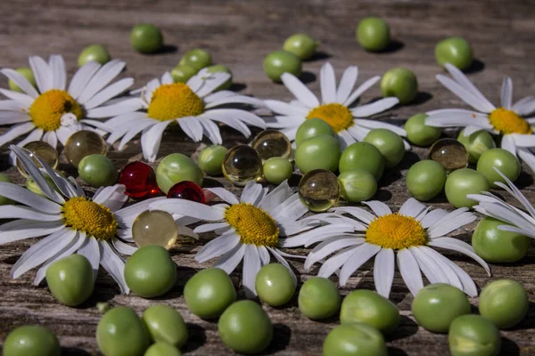 Chamomile green peas and vitamin capsules on an old wooden table ,