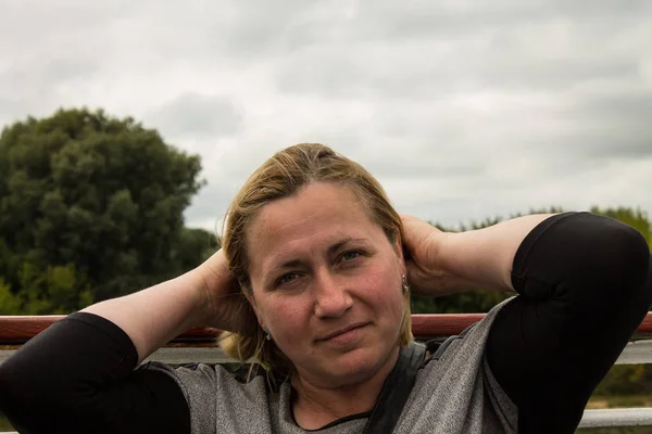 White blonde woman 42 years old with short hair flying in the wind on Board the ship against the river and the banks with green trees and cloudy sky