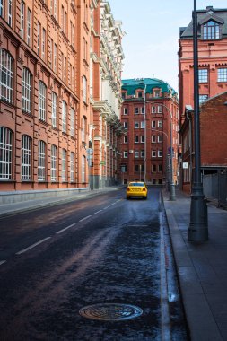 Moskova / Rusya-Eylül 14, 2019: Kırmızı tuğla evler ve ıslak asfalt üzerinde sarı taksi ile tarihi sokak