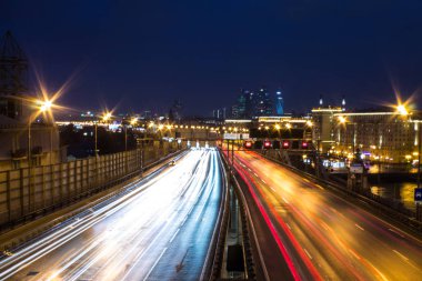 Gece karanlık gökyüzüne karşı farlar ve mimari ışık parlayan hatları ile bir şehir karayolu üzerinde panoramik görünümü