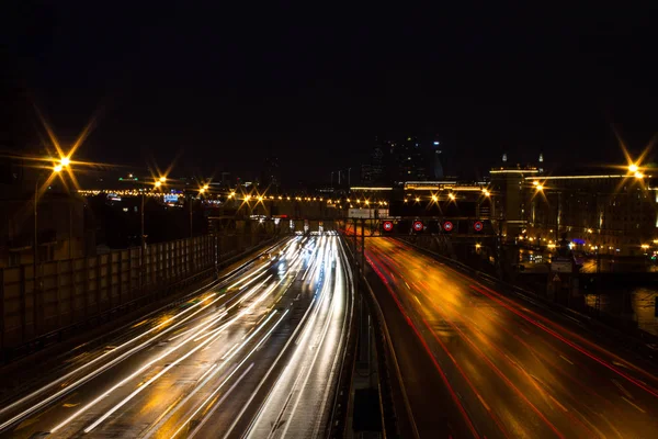 夜の暗い空に対するヘッドランプと建築からの光線の輝く都市高速道路のパノラマビュー — ストック写真