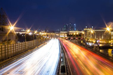 Gece karanlık gökyüzüne karşı farlar ve mimari ışık parlayan hatları ile bir şehir karayolu üzerinde panoramik görünümü