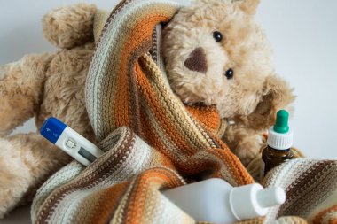 Sıcak bir atkı, ilaç şişeleri ve termometreye sarılmış bir oyuncak ayı.