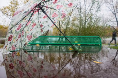 Bulutlu bir sonbahar gününde yağmurda yansıması olan ıslak bir masa tenisi masasında hafif bir şemsiye.