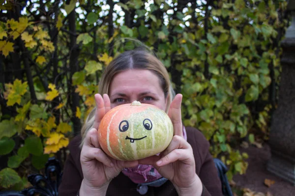 A woman and a pumpkin in her hands with a funny face drawn