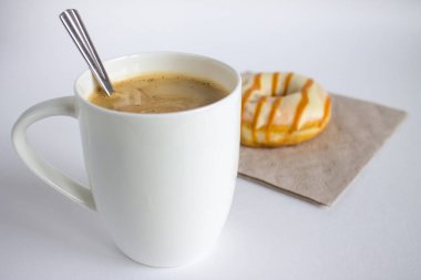 Büyük beyaz kapuçino bardağı ve kremalı donut.