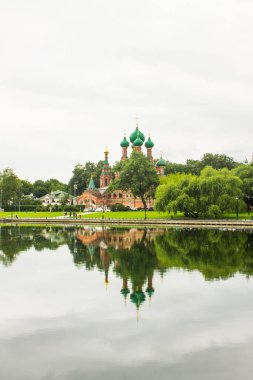 Moskova, Ostankino 'da hayat veren Üçlemeci Kilisesi. Rusya' da bir göletin kıyısında. Bulutlu bir yaz gününde yeşil ağaçların arasında yansıma ve kopyalama alanı.