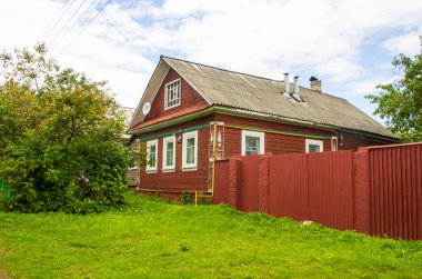 Eski ahşap kulübelerin ve yeşil ağaçların olduğu bir sokak.