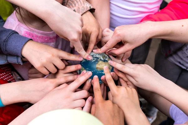 A Group Of Children Holds A Small Toy Globe Of The Earth In Their Hands And Point A Finger At It. Children\'s Hands Point To Different Places On The Globe.