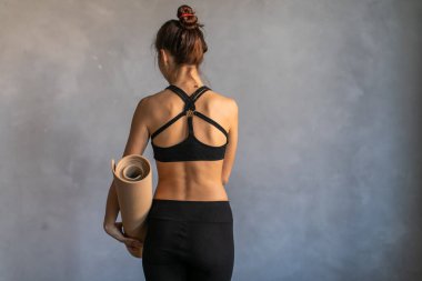 Egzersiz yapan ya da yoga dersinde hasırında paspas olan bir kadın kameraya sırtını döndü. Boşluğu koyu arkaplanda kopyala